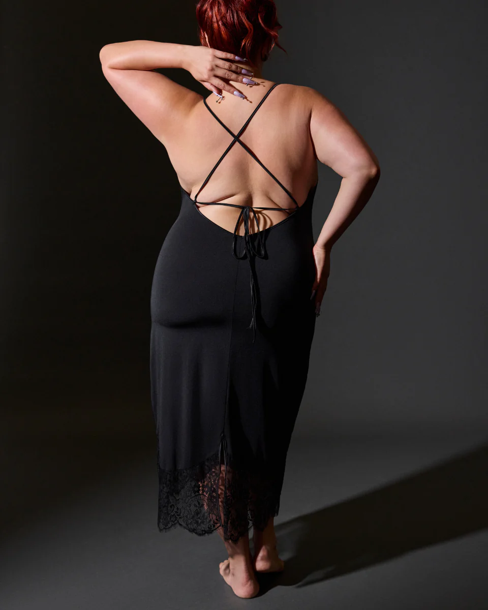 Person wearing a black strappy dress with a dark background