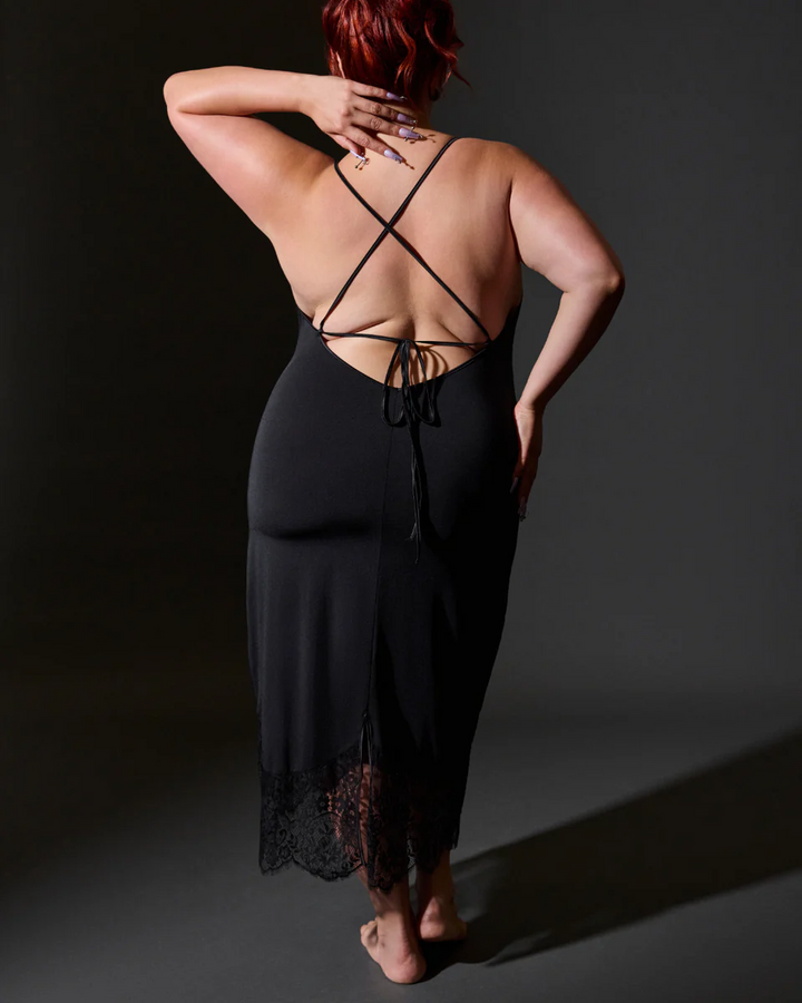 Person wearing a black strappy dress with a dark background