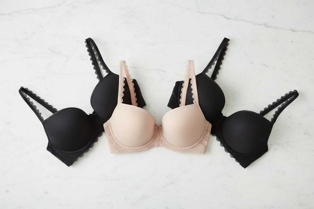 Three underwire t-shirt bras arranged in a row on a white marble surface: two black bras on the sides and one nude beige bra in the center. The bras feature scalloped trim and adjustable shoulder straps.