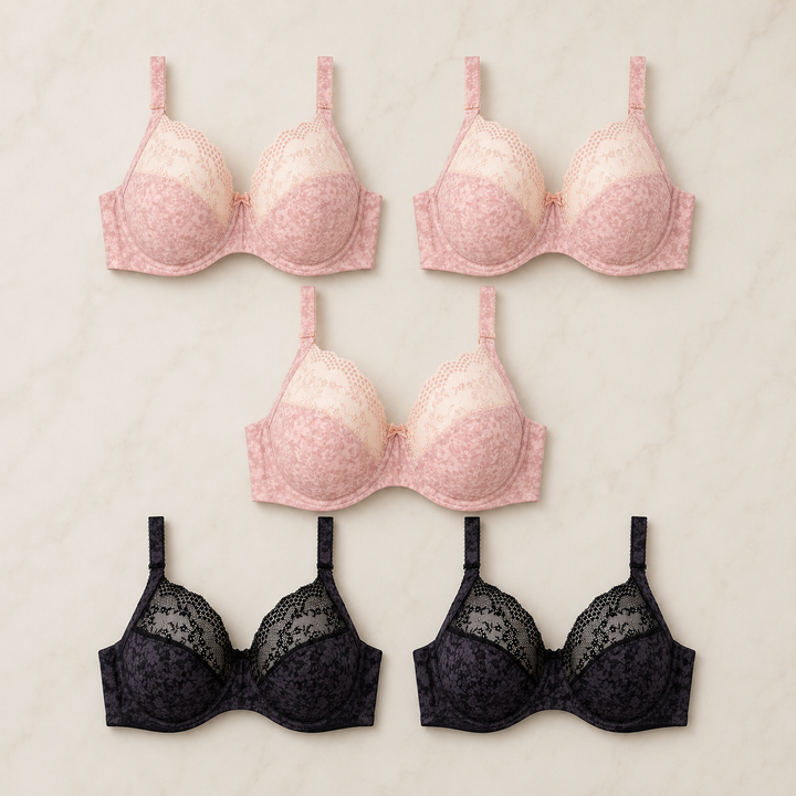 Five large bust underwire bras arranged on a light marble background: two pale blush pink bras at the top and two black lace bras at the bottom.