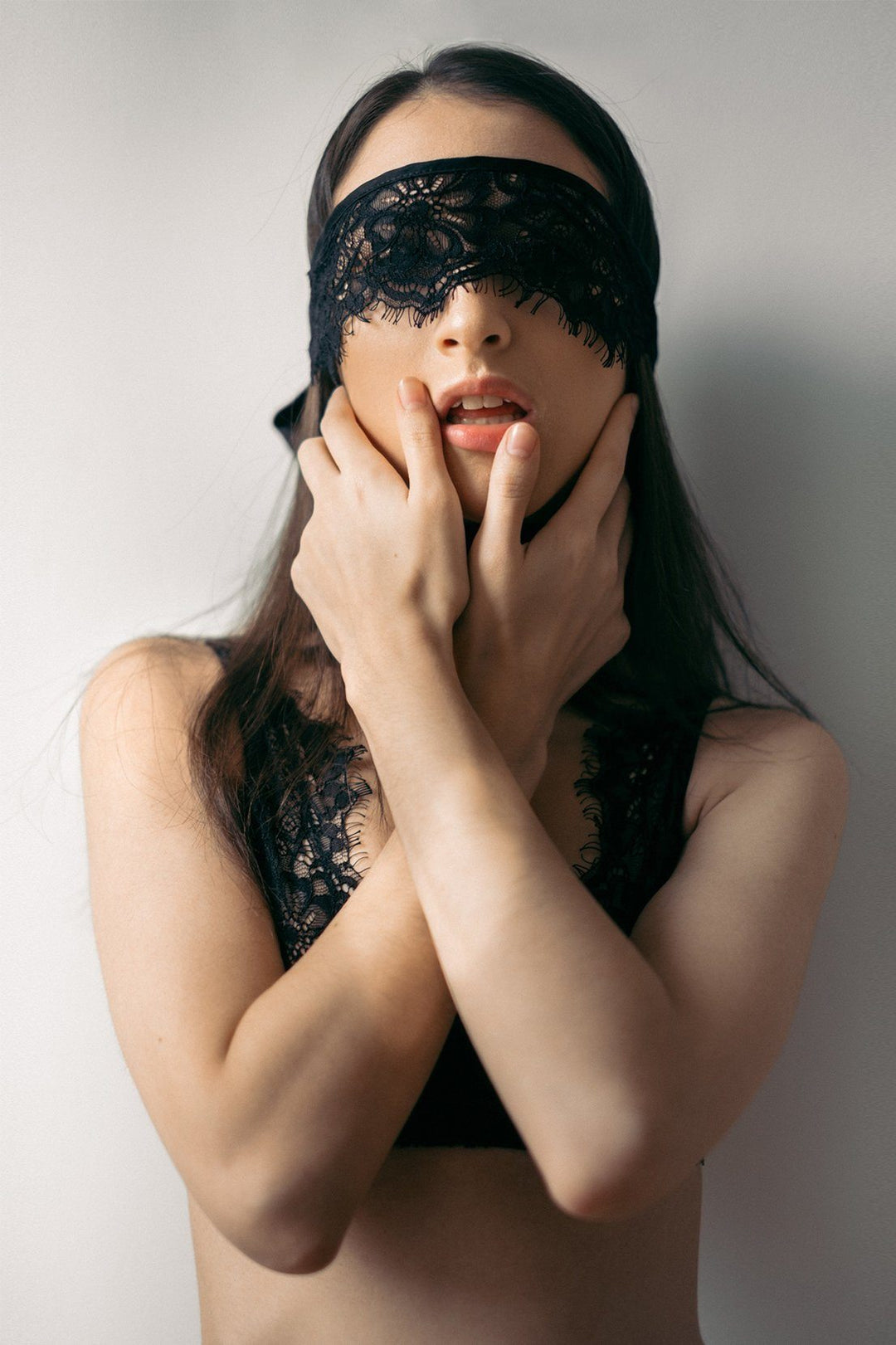 Woman wearing a black lace eye mask against a plain background