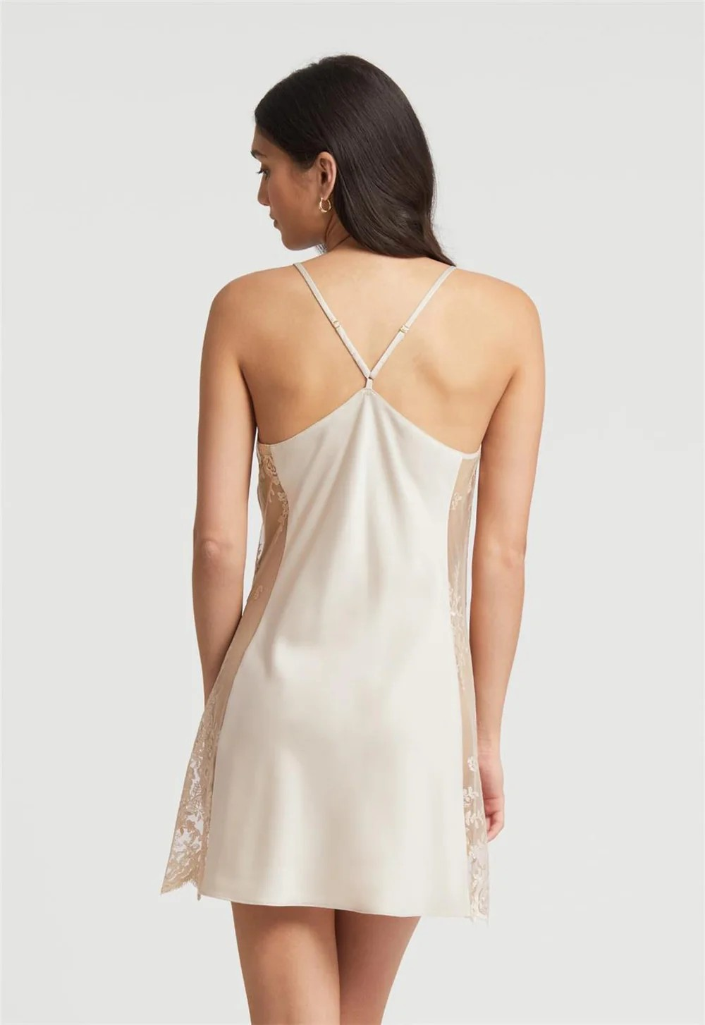 Woman wearing a beige slip dress with lace details on a plain background