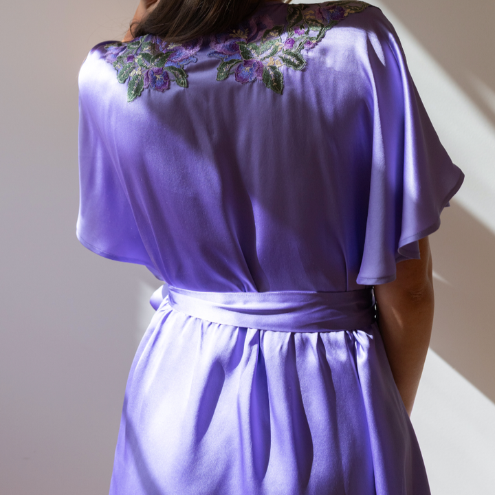 Woman wearing a purple satin robe with floral embroidery on the back.