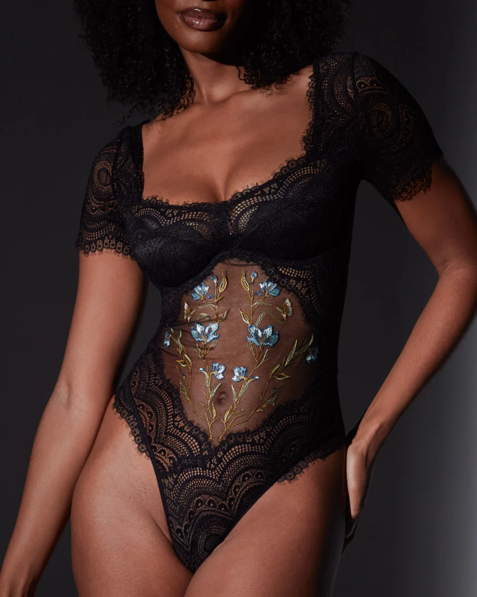 Black lace bodysuit with floral embroidery on a dark background