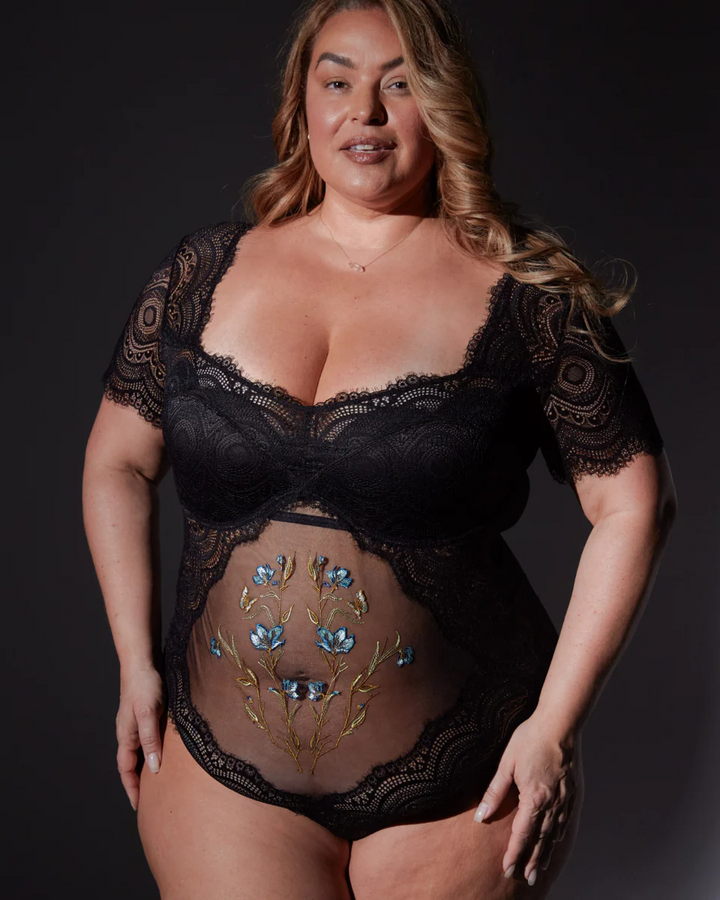 Woman wearing a black lace bodysuit with floral designs on a dark background