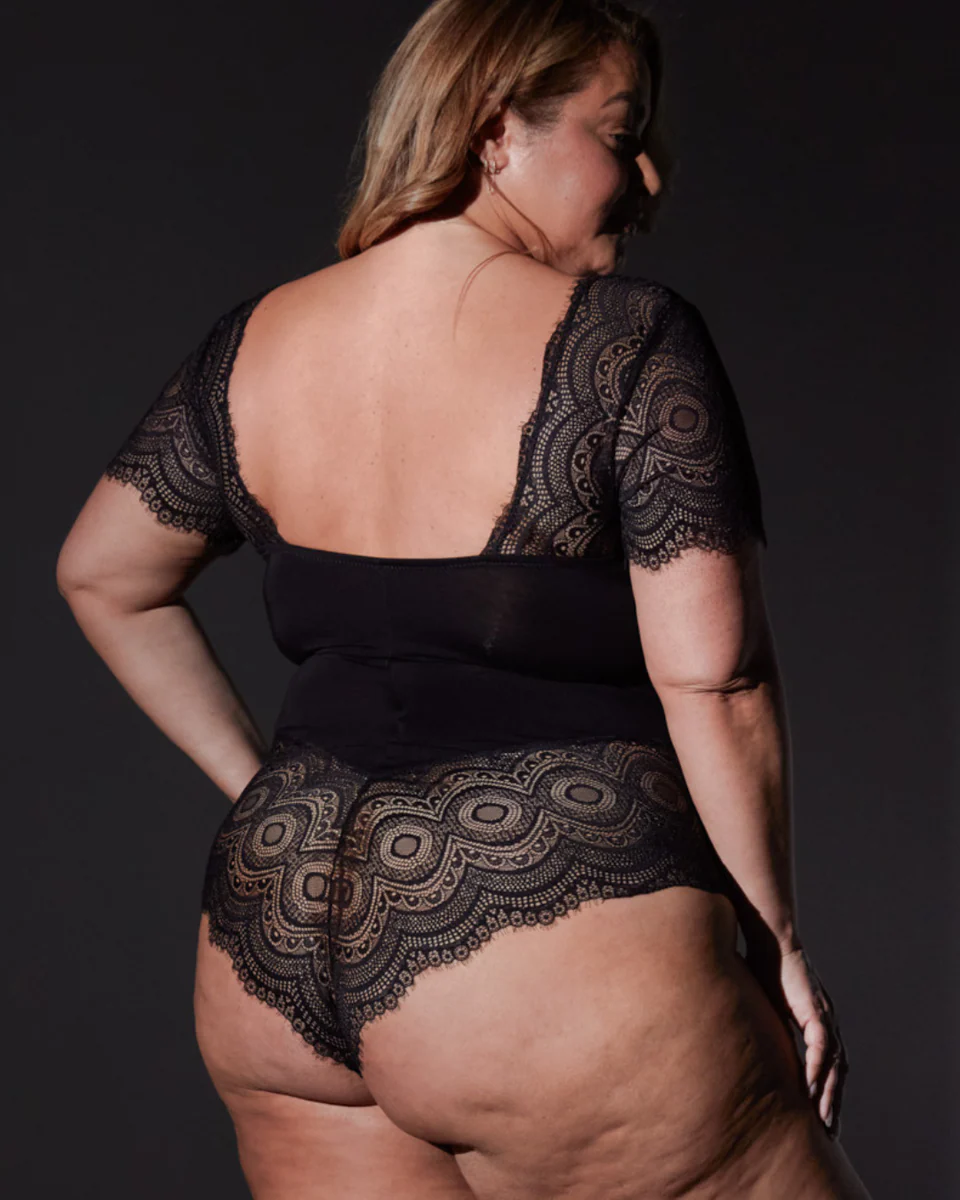 Person wearing a black lace bodysuit against a dark background