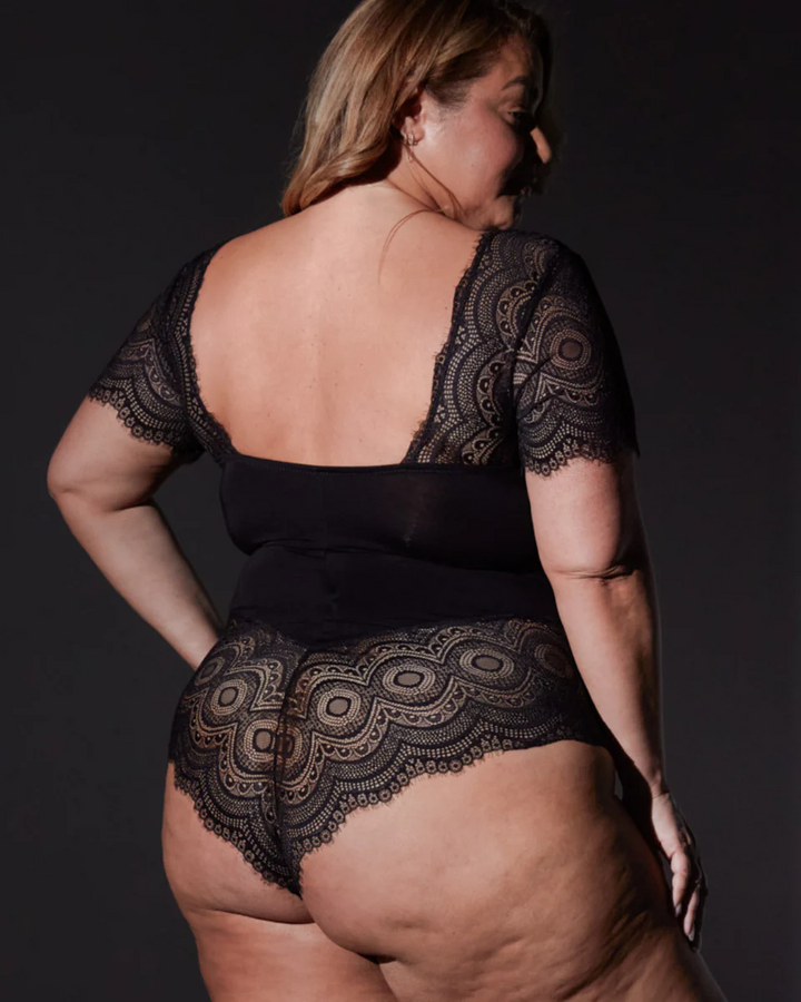 Person wearing a black lace bodysuit against a dark background