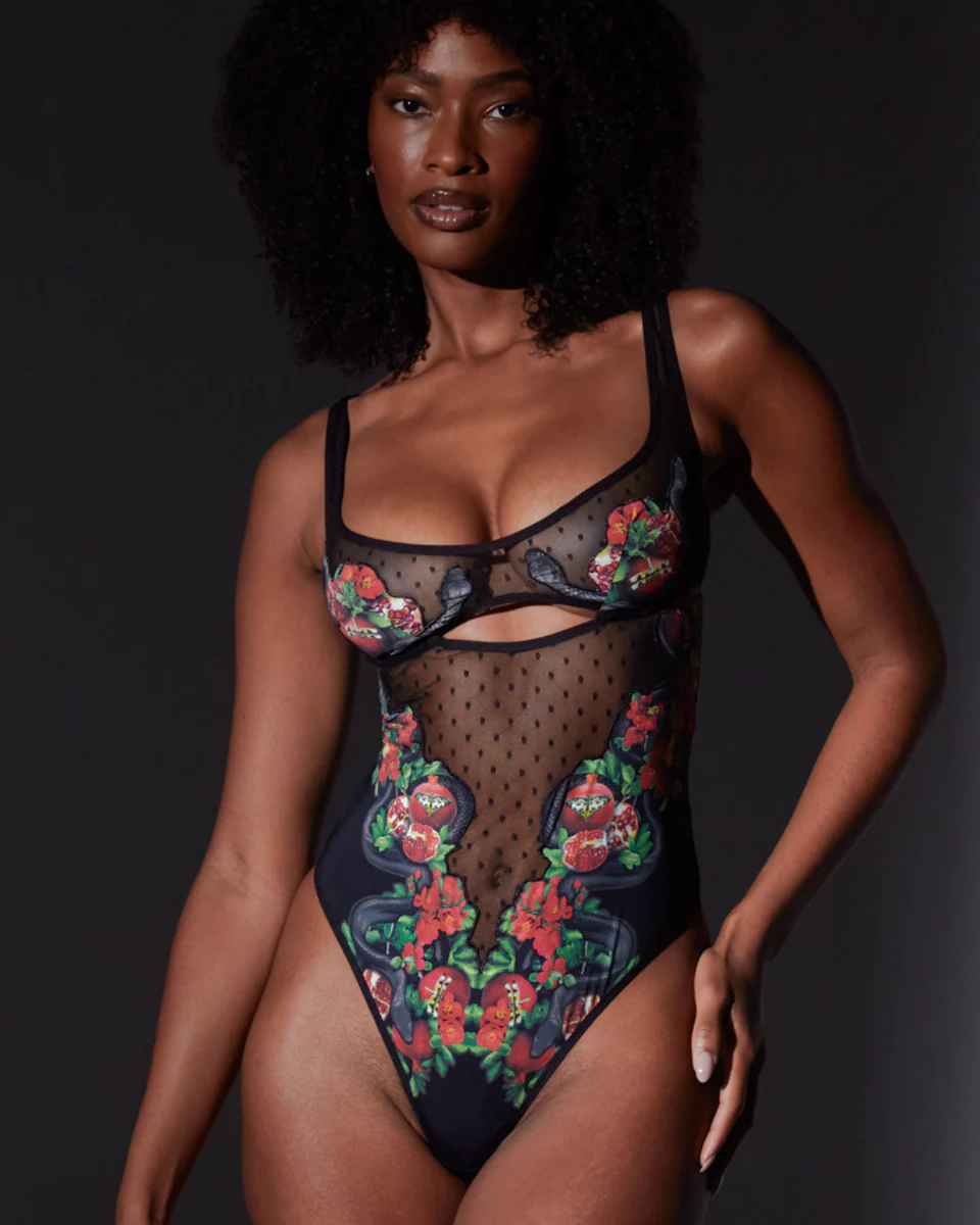 Model wearing a black floral embroidered bodysuit against a dark background