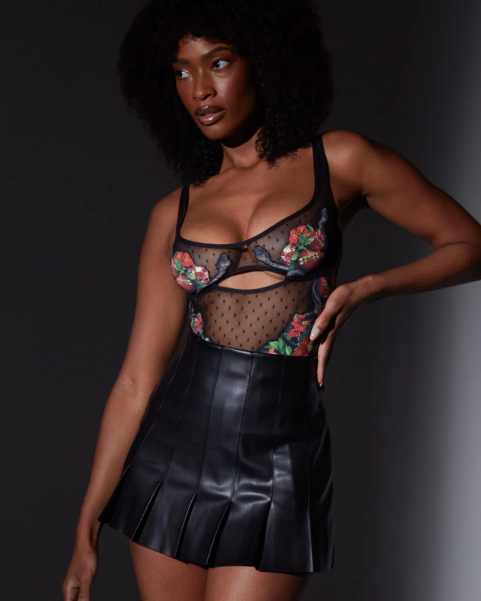 Model wearing a floral mesh top and black leather skirt against a dark background