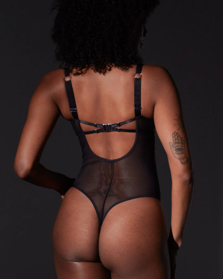 Person wearing a black strappy bodysuit against a dark background