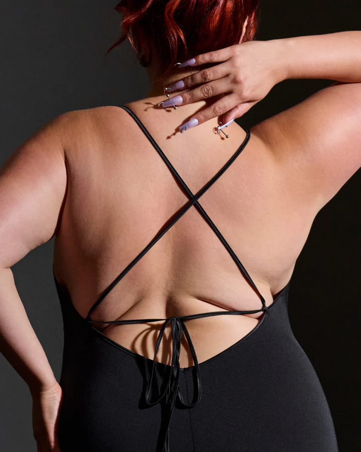 Person wearing a black strappy top against a dark background