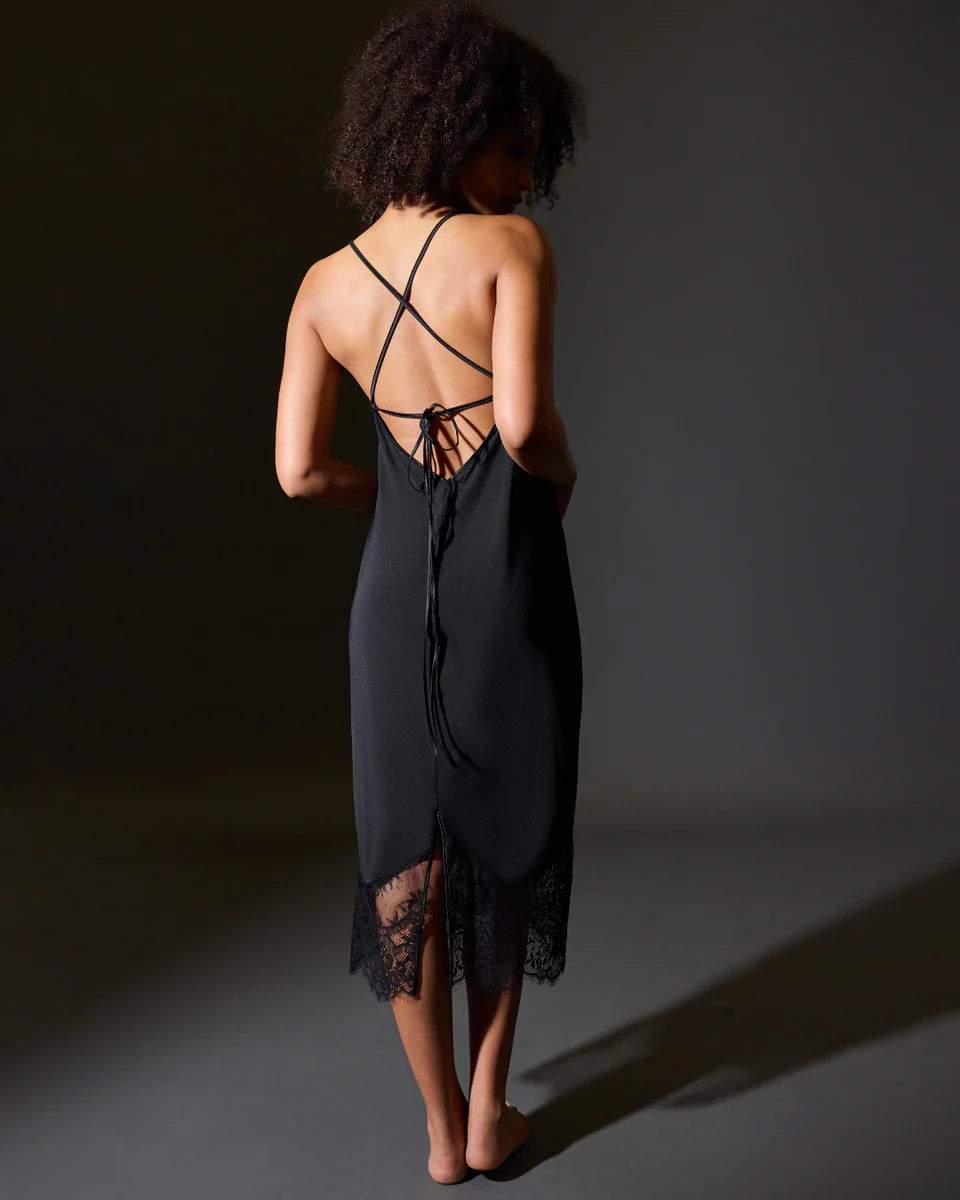 Woman wearing a black slip dress with lace details on a dark background
