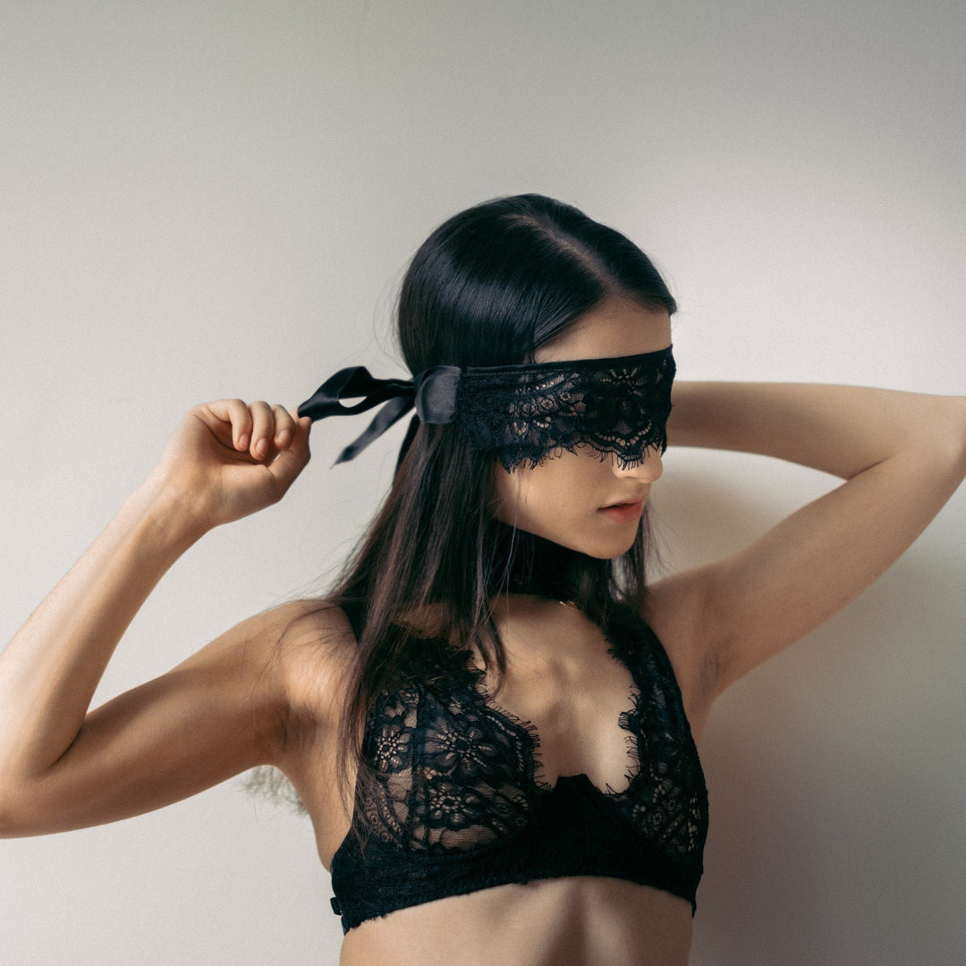 Woman wearing a black lace bra and blindfold against a plain background