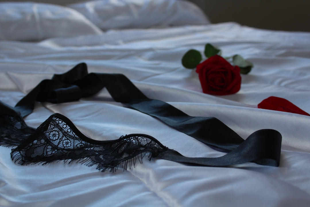 Black lace lingerie and red roses on a white bedspread